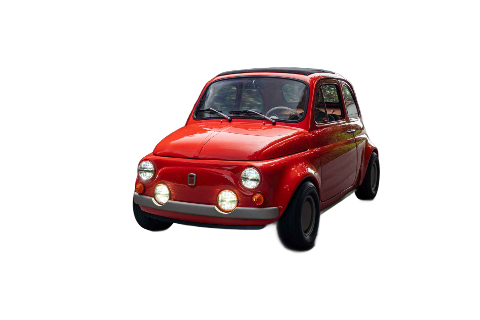 El coche clásico rojo, con un diseño retro, se desplaza por una carretera tranquila flanqueada por una densa vegetación. Su estilo distintivo y faros brillantes lo hacen destacar en el entorno.